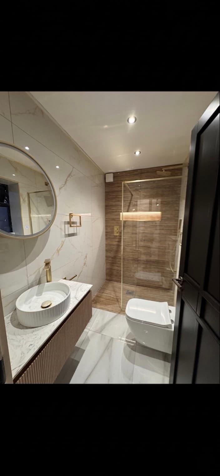 Modern bathroom with marble tiling, gold fixtures, a round mirror, and a glass-enclosed walk-in shower.