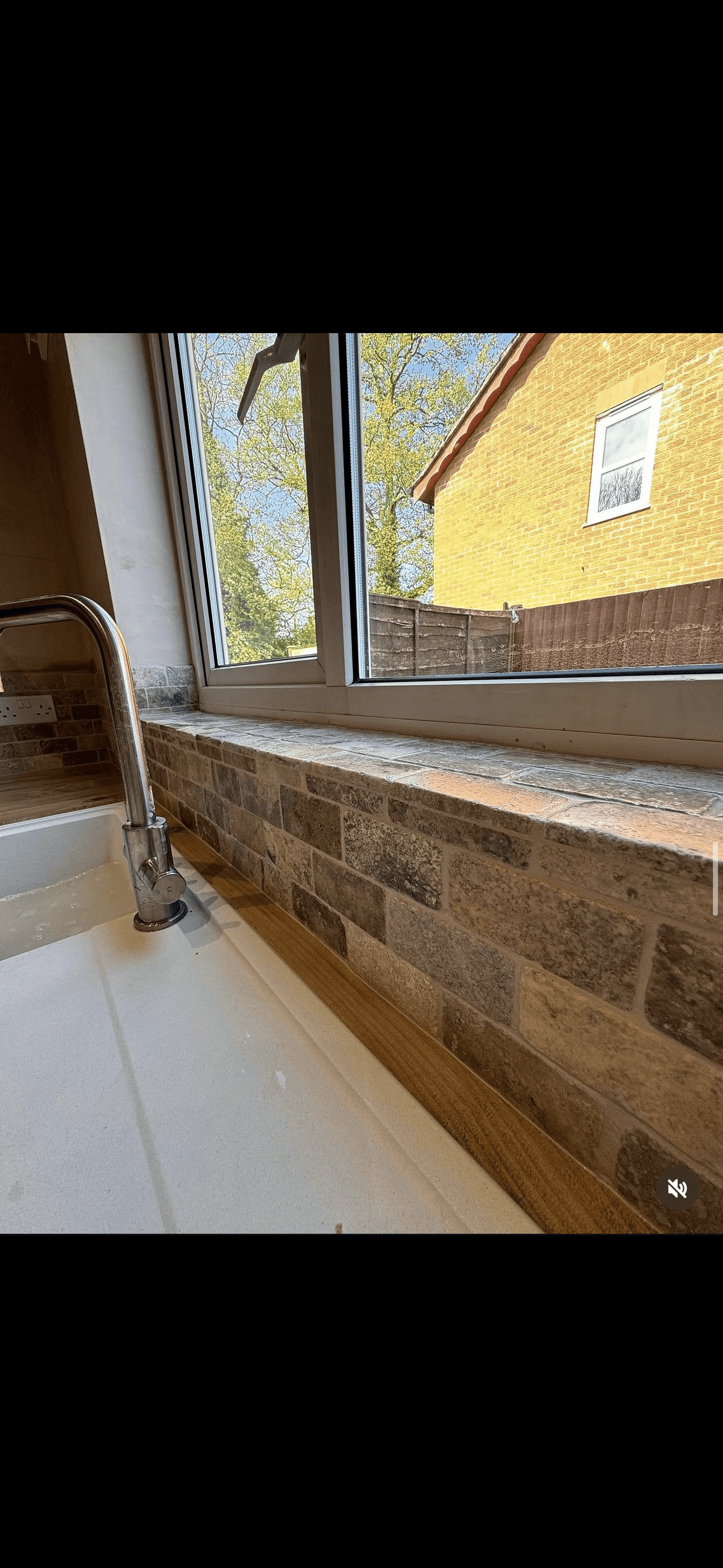 Kitchen sink with chrome faucet and stone-effect tiles on the backsplash and windowsill.