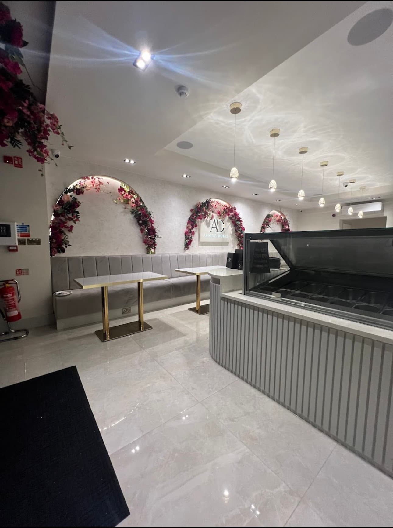 Elegant dessert shop featuring grey velvet seating, floral wall arches, and modern service counter.