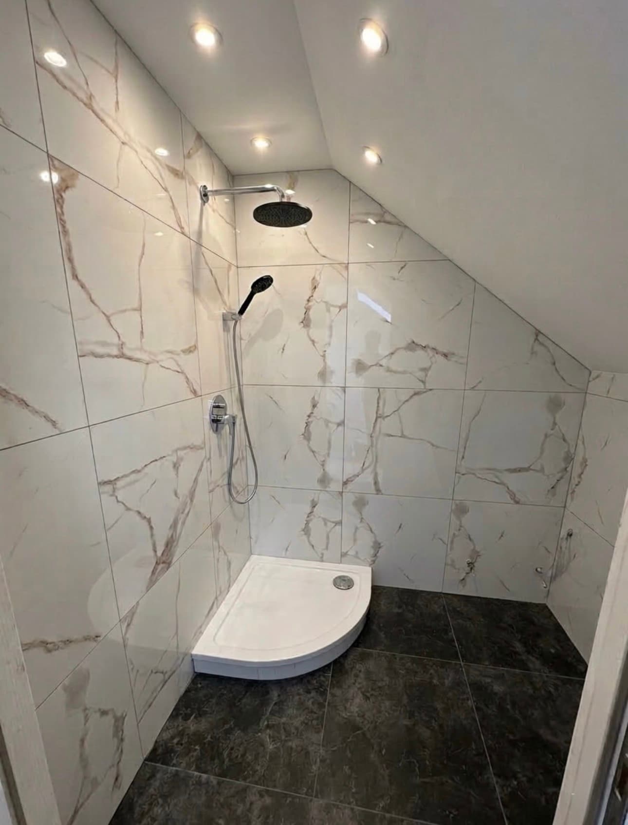 Modern shower with white marble-effect walls, dark floor tiles, and a curved white tray.