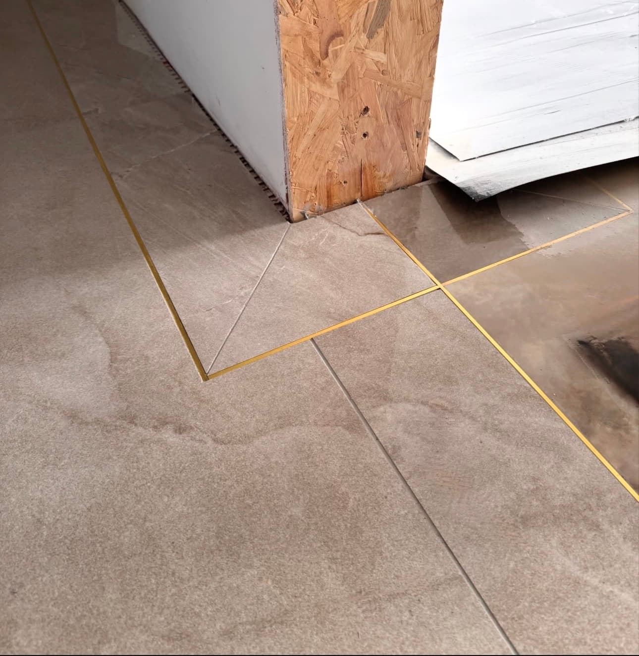 Large beige stone tiles with gold metal inlay strips precisely cut around a wall corner.