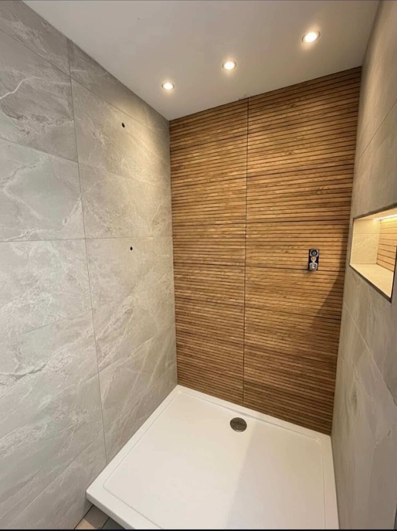Modern walk-in shower with gray marble tiles, a wood-slat accent wall, and recessed ceiling lights.