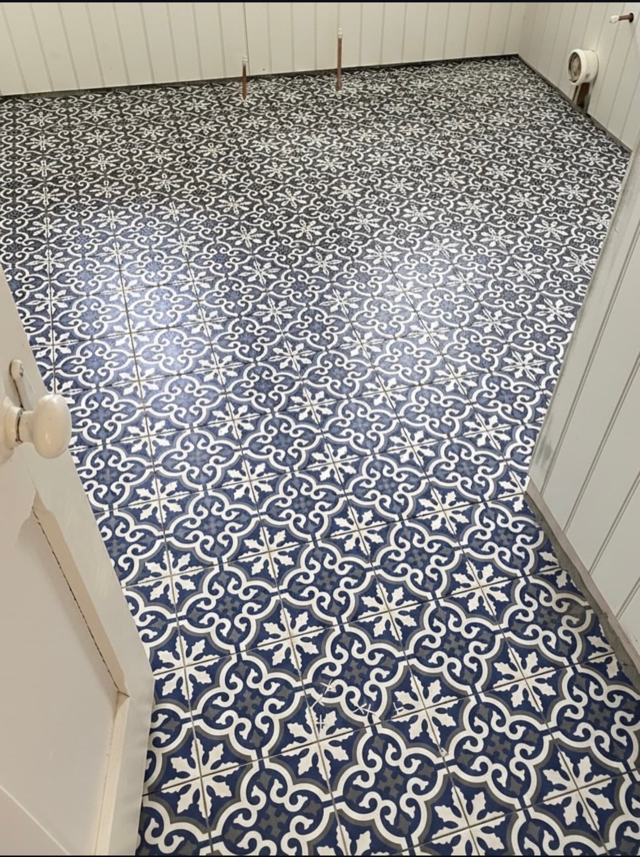 Intricate blue and white patterned floor tiles in a room with white vertical wood paneling.