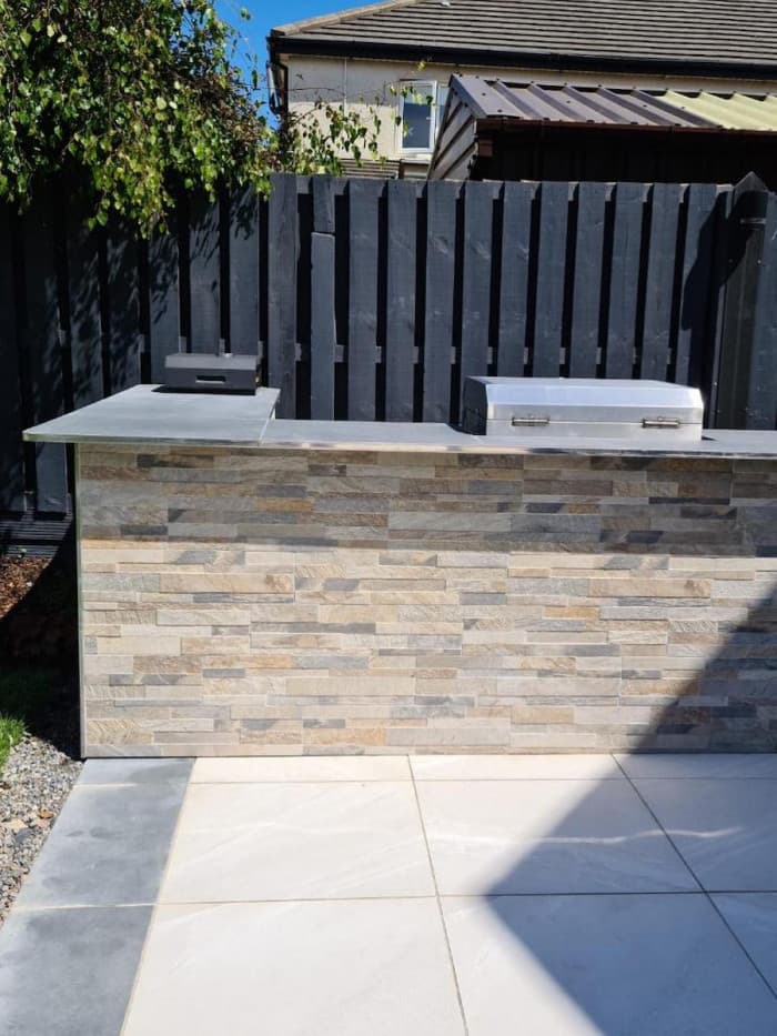 Modern outdoor kitchen with stacked stone base, grey countertop, and built-in stainless steel grill.
