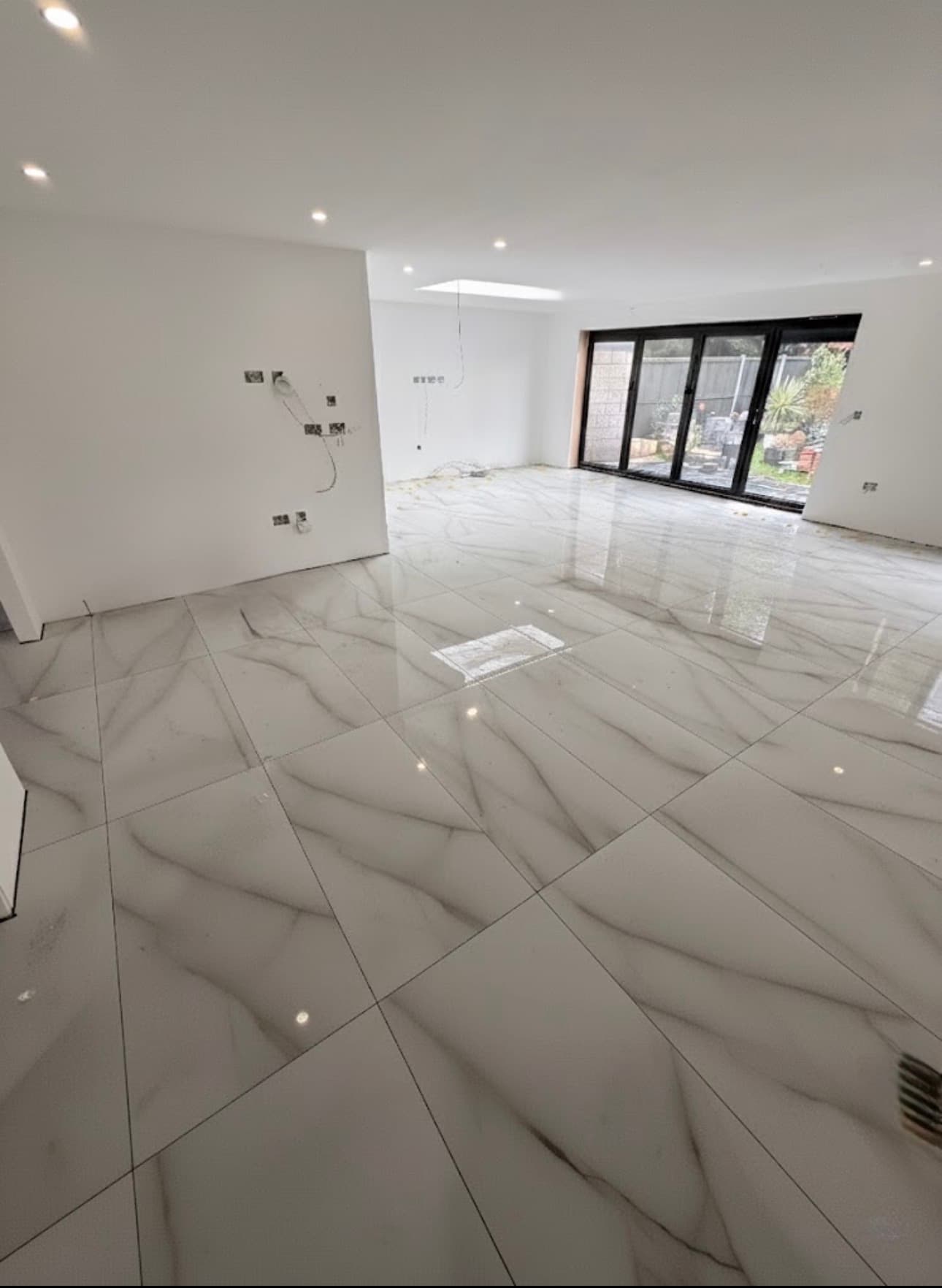 Bright room featuring glossy white marble floor tiles and large black-framed glass doors.
