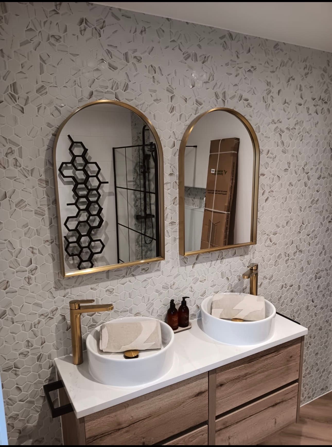 Modern bathroom vanity featuring vessel sinks, gold faucets, and arched mirrors against hexagonal tiles.